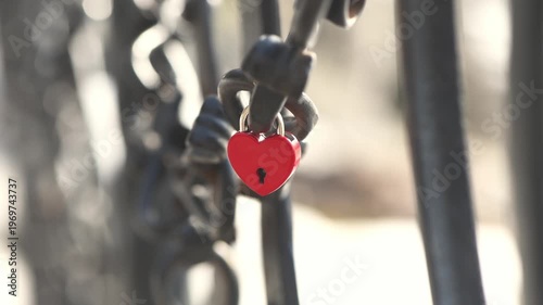 Red heart shaped padlock securely fastened to a metal chain, representing eternal love, commitment, and lasting romance with soft bokeh creating a romantic atmosphere