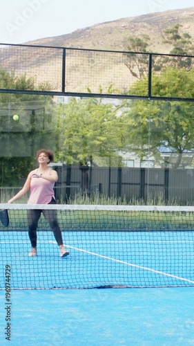 Vertical video: Returning player in pink top hitting incoming green ball with paddle on blue court