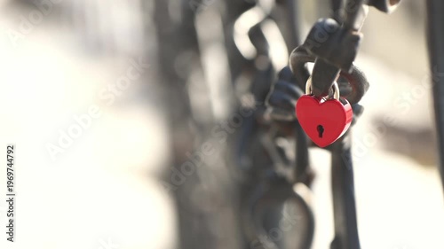 Red heart shaped padlock securely fastened to a metal chain, representing eternal love, commitment, and lasting romance with soft bokeh creating a romantic atmosphere