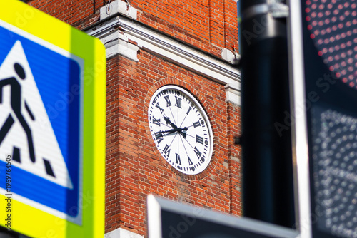 Close-up of a large outdoor clock with Roman numerals on a red brick tower building. The clock tower of the Cherepovets Chamber Theater, a landmark of urban architecture.