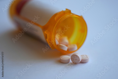 An orange prescription bottle tipped over, spilling pills on white background. Macro side view with copy space. Healthcare medical concept.