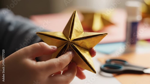Child's hands carefully assemble a golden origami star, showcasing intricate folds and details, with colorful paper and crafting tools visible in the background