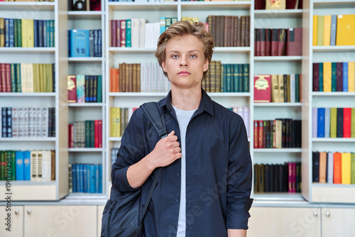 Portrait of serious teenage student with backpack in classroom library