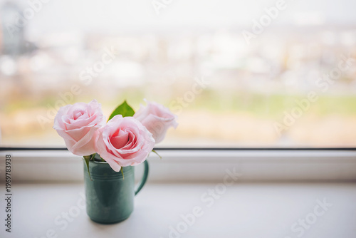 Three delicate pink roses bloom gracefully in a green vase, placed by a sunny window. Soft sunlight filters through, illuminating the flowers and creating a serene atmosphere