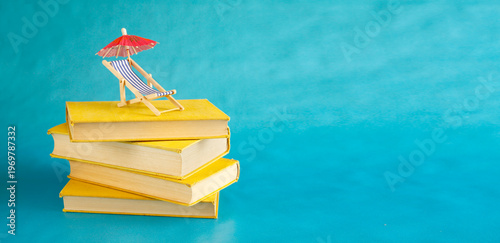 stack of books with deckchair and sun umbrella, spring and summer holiday read. Vacationsummer holidays,,travel, inspiration,relaxation with books,reading and literature concept.
