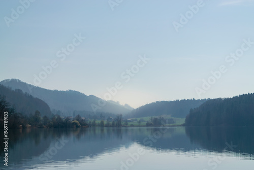 Wide landscape view of a tranquil lake reflecting forested hills, rural valley, clear blue sky, serene natural panorama - Türlersse, Switzerland