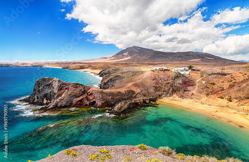 Turquoise bay and sandy beach curve beneath volcanic hills and dramatic clouds at Playa del Papagayo, Lanzarote, Canary Islands.