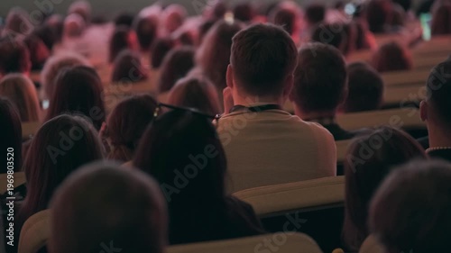Panoramic view of business conference audience seated in auditorium, rear view of attendees in soft low light, focused atmosphere, networking, learning, professional event energy