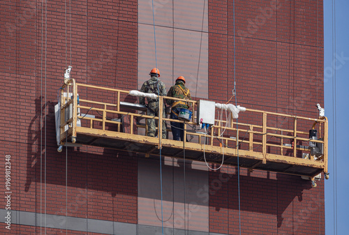 At the construction site. Workers in a high-altitude dolly are finishing the facade