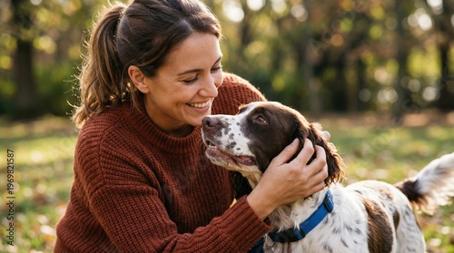 Happy young woman bonding with English Springer Spaniel dog in autumn park. Cheerful female pet owner enjoying outdoor leisure with her loyal puppy. Domestic animal care and friendship.