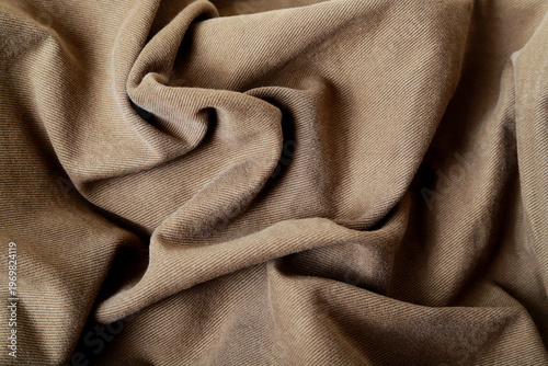 Rough-textured brown denim fabric arranged in deep waves. A background for graphic design projects.