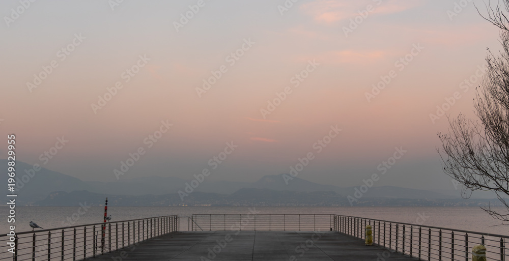 Fototapeta premium Empty pier on Lake Garda at sunset with mountains and calm water, Italy