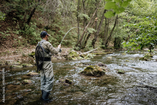 Tableau sur toile A male angler wearing waders stands in a shallow woodland stream while fly fishing and casting a rod during a peaceful outdoor adventure in nature