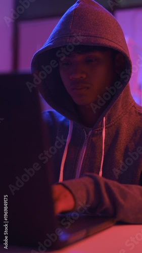 A mysterious hooded hacker working on a computer in a dark room.