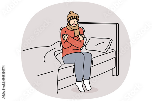Freezing man is shaking sitting on bed and feeling chills and cold, dressed in hat and scarf. Freezing guy suffers due to lack of central heating system and poor immunity, located in bedroom