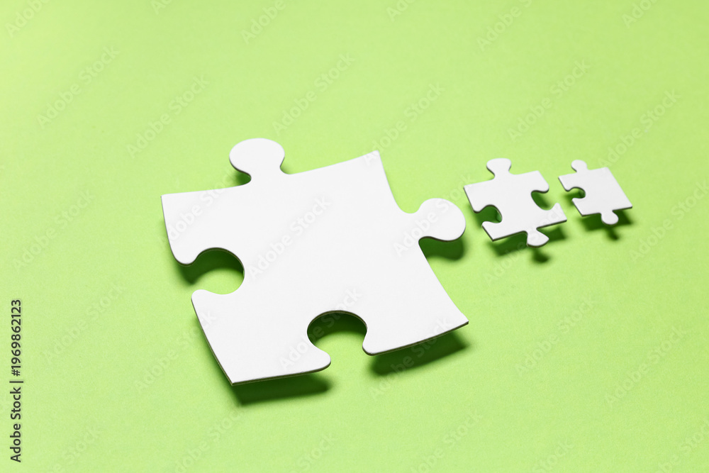 Fototapeta premium Pieces of white jigsaw puzzle on green background