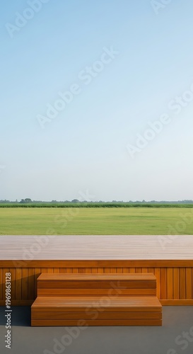 Modern wooden stage platform with steps set against a vast green field and clear blue sky a serene outdoor setting for events or performances