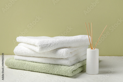 Obraz na plátně Stack of clean towels and reed diffuser on light table near color wall