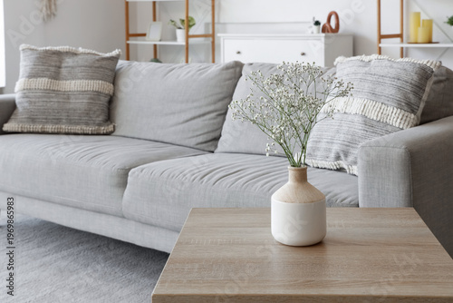 Vase with flowers on table near sofa in living room