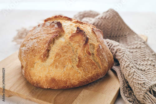 Golden sourdough loaf on wooden board with knit Linen Towel and glass of milk. Ideal for culinary, baking, and food lifestyle content.