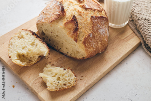 Sliced artisan sourdough bread with airy crumb on wooden board, glass of milk, and knitted cloth. Ideal for culinary, baking, and food photography projects.
