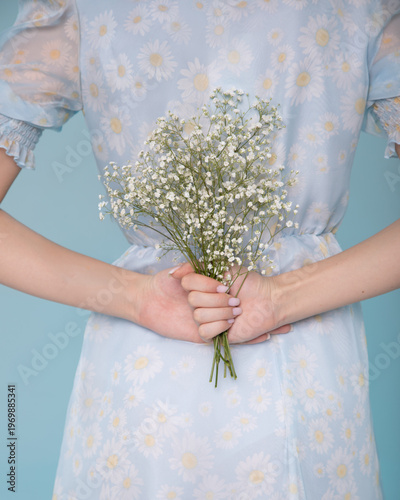 Woman hides gypsophila bouquet behind back in blue dress with flowers