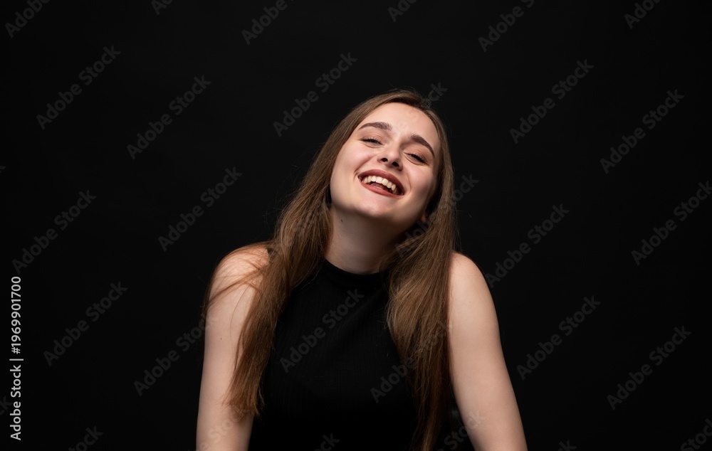 Fototapeta premium Happy young woman posing on a black background, expressing joy and laughter with a positive emotion and vibrant energy