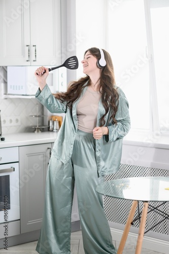 Happy Woman in Pajamas Singing into Spatula as Microphone in Kitchen, Dance While Listening to Music in Headphones. Joyful Morning Routine, Positive Lifestyle Concept, Leisure, Mental Health Wellness