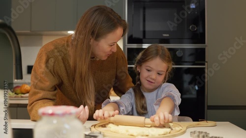 Mother and daughter rolling dough and making cookies in a bright kitchen