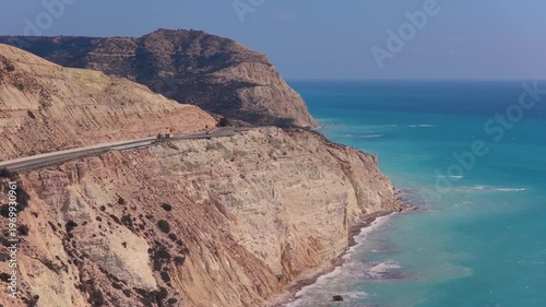 Aerial drone view of a winding coastal road running along steep white cliffs above the turquoise Mediterranean Sea in Cyprus