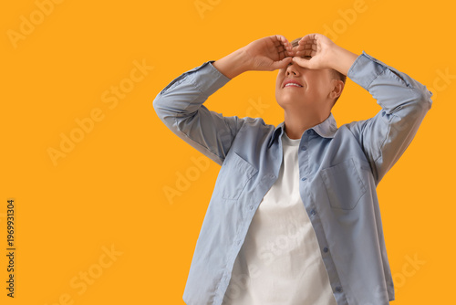 Young woman looking through imaginary binoculars on yellow background