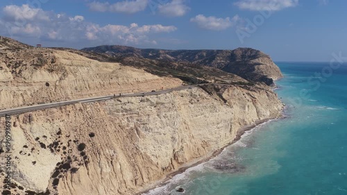 Aerial drone view of a winding coastal road running along steep white cliffs above the turquoise Mediterranean Sea in Cyprus
