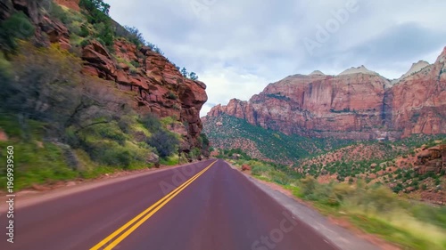 An eye-level perspective shot from a moving vehicle captures the experience of driving along the famous Utah State Route 9 in Zion National Park. The footage showcases the majestic, towering red and o