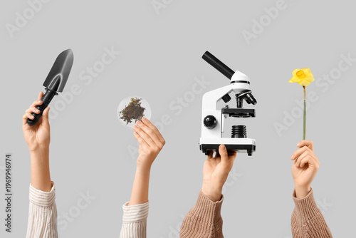 Female hands with modern microscope, gardening shovel, daffodil flower and Pe...