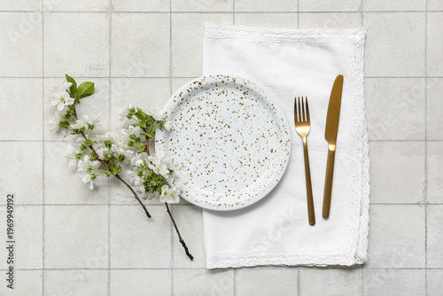 Beautiful table setting with golden cutlery and blooming branches on white tile background