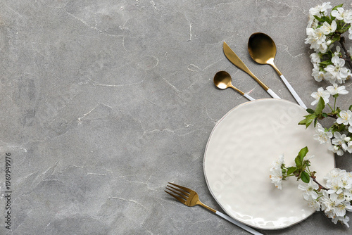 Beautiful table setting with golden cutlery and blooming branches on grey background