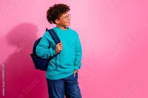 Obraz na plátne Smiling schoolboy with backpack looking to the side against a pink background, c