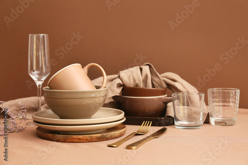 Stack of clean dishes with golden cutlery and gypsophila flowers on brown background