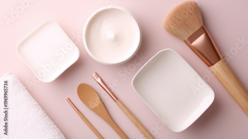 A flat lay of skincare utensils including containers, a brush, and wooden tools on pink background