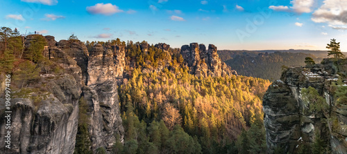 Huge panorama of the jagged Bastei rock formations, including the Wehltürme and the Ferdinandstein lookout, where a visitor admires the Saxon Switzerland landscape on a winter sunrise.