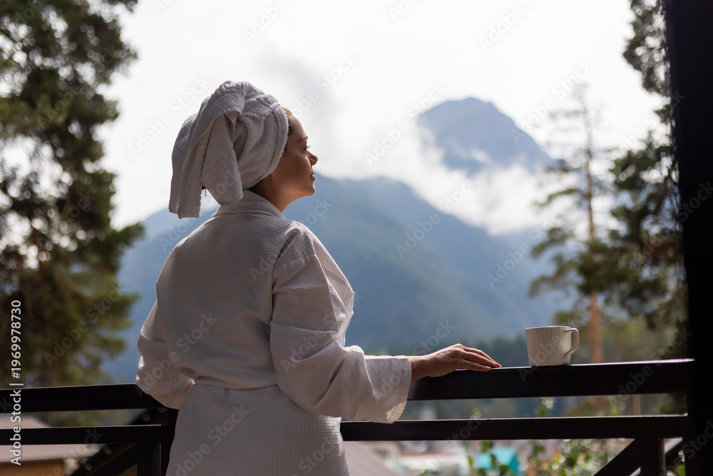 Fototapeta premium woman in a white robe and a towel on her head, with mountains in the background, in a hotel