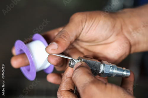 Εκτύπωση καμβά Close-up of mechanic hands wrapping white teflon seal tape on a hydraulic fitting connector thread in a workshop to prevent leaks