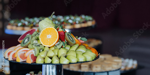 A vibrant buffet display featuring fresh fruit slices, canapes, and pastries arranged on tiered stands.