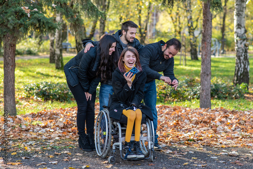 Young woman using a wheelchair taking selfie with friends in a park