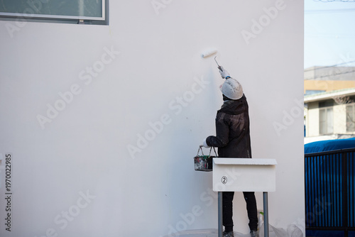 家の外の壁をペンキを塗る男性作業員の姿