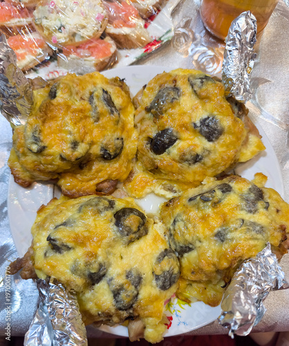 Roasted poultry legs topped with melted golden cheese and dark mushroom slices featuring aluminum foil wrapped bone handles served on festive dinner plate alongside salmon sandwiches.