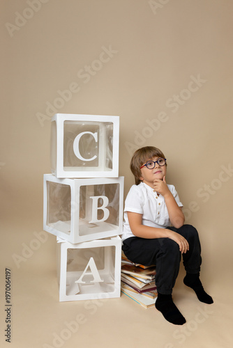 Thoughtful boy with glasses sitting on books with alphabet blocks