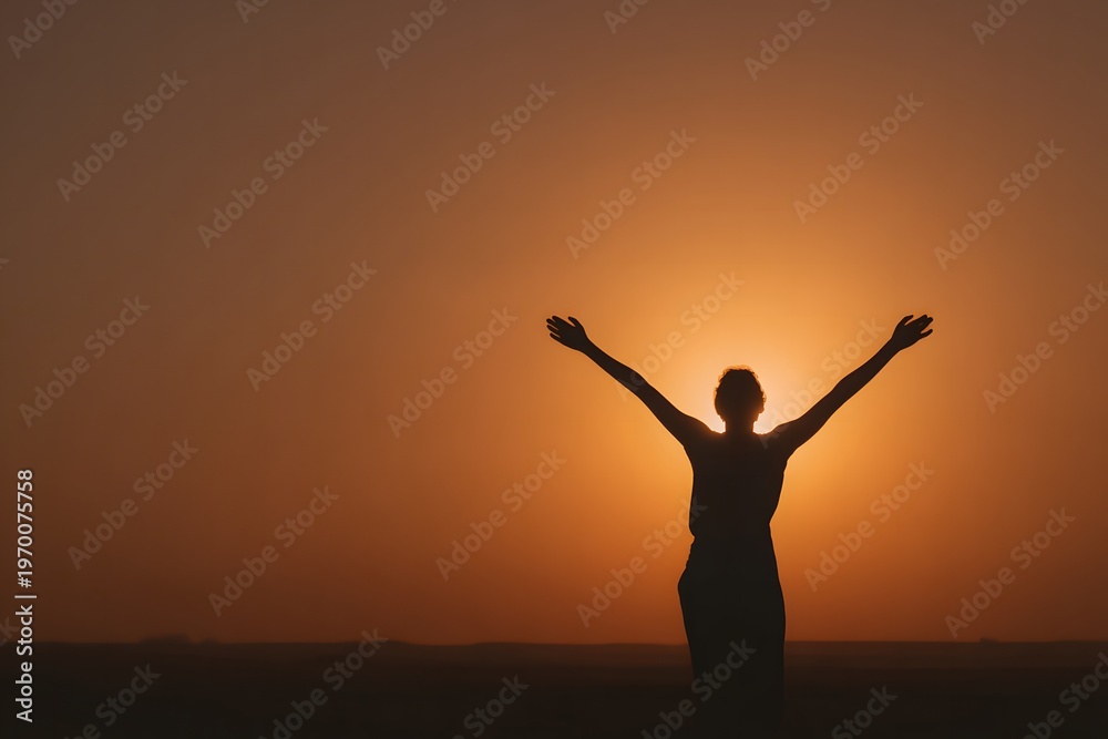 Fototapeta premium Silhouette of a person standing with raised arms facing the golden sunrise