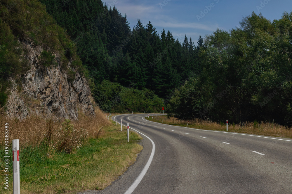 Fototapeta premium Winding Mountain Road Through Lush Forest and Rocky Terrain on Sunny Day