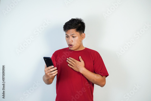 Fotografía Surprised Young Asian Man Looking At Phone In Red T-Shirt Reacting To Shocking M